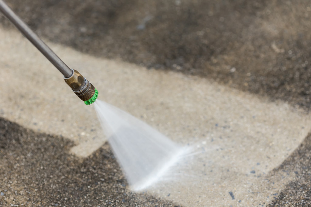 Close-up view of a pressure washer nozzle spraying water onto a concrete surface, creating a clean streak.